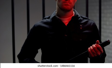 Aggressive Warden Holding Truncheon Standing Against Prison Cell, Red Lights