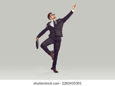 Agile energetic office worker dancing isolated on grey background Full body length shot young business man in classic suit and tie holding diplomat case and doing graceful pirouette like ballet dancer