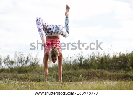 Agile young woman doing a handstand outdoors in the countryside balancing on her hands with her legs bent in opposite directions