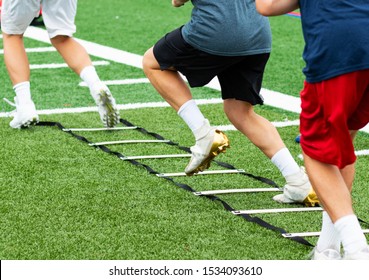 An agility ladder is on a green turf field with three young boys in cleats running through each leg. - Powered by Shutterstock