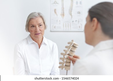 Aging and back pain concept: doctor of rheumatolgy showing her senior patient a slipped disk on a backbone model.