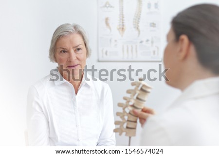 Aging and back pain concept: doctor of rheumatolgy showing her senior patient a slipped disk on a backbone model. Stock photo © 