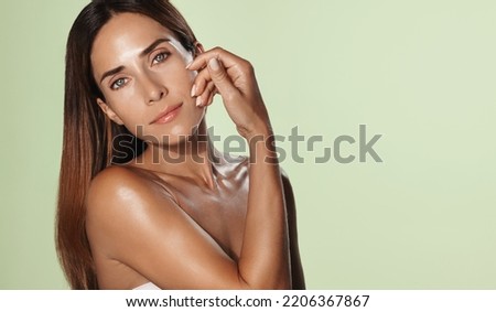 Aging beauty. Woman 50 years old with healthy hair, hydrated facial skin without wrinkles, gently touches her face, has glowing body after washing in shower, green background.