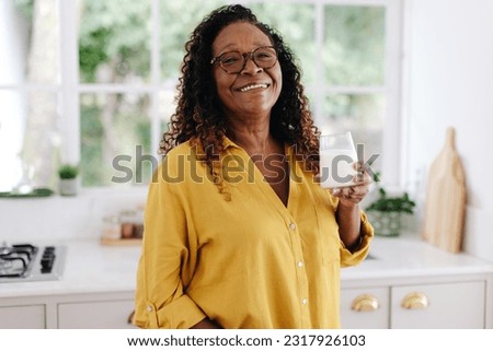 Aging black woman drinking a glass of fresh milk for breakfast, knowing that it's an important part of a balanced diet. Happy senior woman taking care of her health with her dairy product.