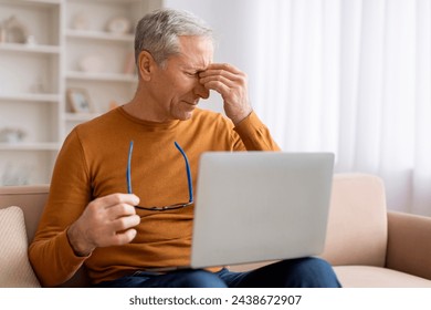 Aging eyes concept. Senior retired man grandfather rubbing eyes and holding eyeglasses while using laptop at home, sitting on couch, reading news, scrolling, websurfing. Vision care for seniors - Powered by Shutterstock