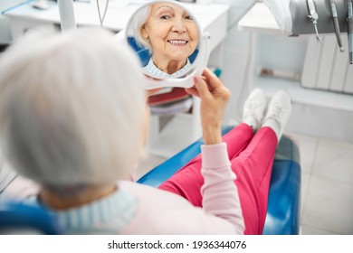 Aging Female Checking Her Teeth In Mirror From Dental Chair