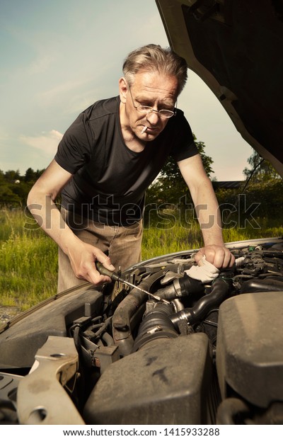Aging\
man trying to fix broken car engine on lonely\
way
