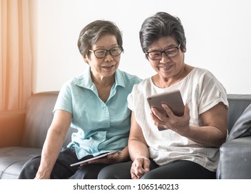 Aging society concept with Asian elderly senior adult women (twin sisters) using mobile tablet application technology for social network among friends community via internet digital communication