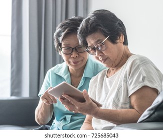 Aging society concept with Asian elderly senior adult women (twin sisters) using mobile tablet application technology for social network among friends community via internet digital communication 