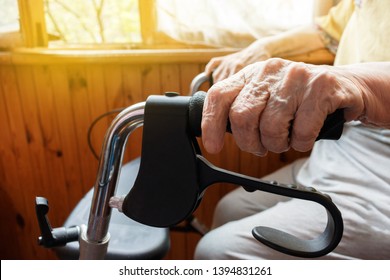 Aging woman holds her wrinkled hand on an adult medical walker sitting on the balcony in bright sunshine. Aging process and old age - old senior woman’s hand with wrinkled skin and veins