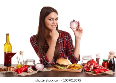 Agirl sits at a table with a meal and holds a half of onions in her hand and smiles. Isolated on white.