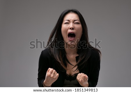 Agitated upset woman yelling in anguish or frustration with clenched fists over a grey studio background with copyspace