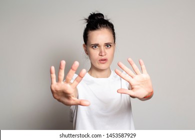 An Agitated Young Woman Put His Palms Forward As Protection, Calming Someone Down And Looking Anxiously At The Camera. Isolated On White Background. Close-up.