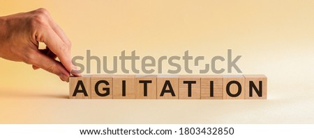 AGITATION word made with building blocks. Hand holding wooden cube block with AGITATION business word on yellow background