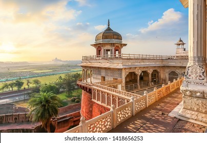 Agra Fort - Medieval Indian fort made of red sandstone and marble with view of dome at sunrise. View of Taj Mahal at a distance as seen from Agra Fort.