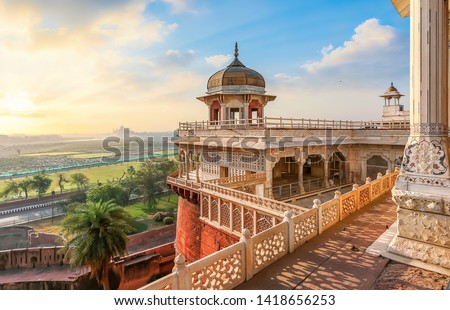 Agra Fort - Medieval Indian fort made of red sandstone and marble with view of dome at sunrise. View of Taj Mahal at a distance as seen from Agra Fort.