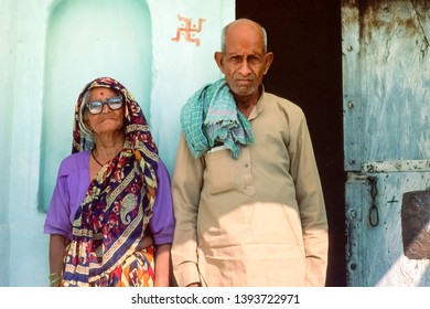 Agra, Uttar Pradesh/ India - November 1998: Portrait Of An Elderly Couple, Traditional Clothing, Standing At The Door In Front Of Their House, Religious Symbol Painted On The Wall