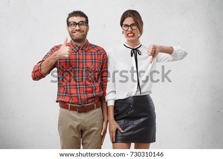 Agree and disagree concept. Two male and femae friends express different emotions as evaluate something. Cheerful wonk man raise thumb shows ok sign. Unpleased female model expresses dislike