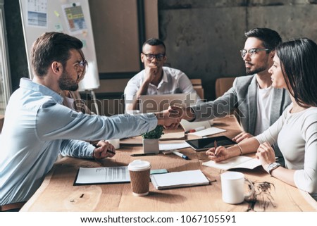 Agreement.  Young modern men in smart casual wear shaking hands while working in the creative office
