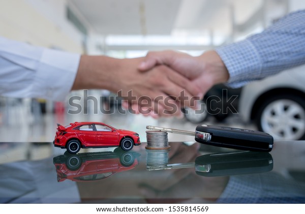 Agreements to buy new cars,\
new car loans or signing contracts with car keys and money in the\
foreground Blurred background for two business people standing hand\
in hand