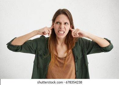 Agressive female plugging her ears being angry with her neighbours who are very noisy. Irritated beautiful young woman trying to avoide loud sounds from house next door hating creaking sounds