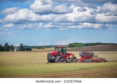 Agricultural Background With Red Tractor Pulling Plow, Throwing Dust In Air. Combine Harvester At Wheat Field. Heavy Machinery During Cultivation, Working On Fields. Dramatic Sky, Rain, Storm Clouds
