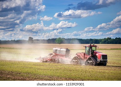 Agricultural Background With Red Tractor Pulling Plow, Throwing Dust In Air. Combine Harvester At Wheat Field. Heavy Machinery During Cultivation, Working On Fields. Dramatic Sky, Rain, Storm Clouds
