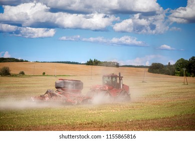 Agricultural Background With Red Tractor Pulling Plow, Throwing Dust In Air. Combine Harvester At Wheat Field. Heavy Machinery During Cultivation, Working On Fields. Dramatic Sky, Rain, Storm Clouds
