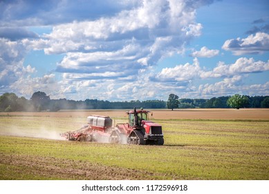 Agricultural Background With Red Tractor Pulling Plow, Throwing Dust In Air. Combine Harvester At Wheat Field. Heavy Machinery During Cultivation, Working On Fields. Dramatic Sky, Rain, Storm Clouds
