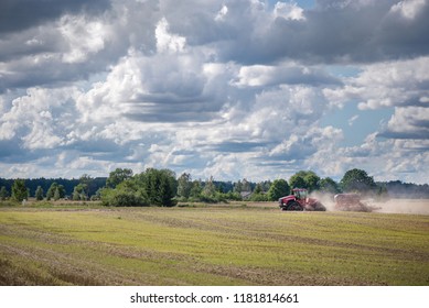 Agricultural Background With Red Tractor Pulling Plow, Throwing Dust In Air. Combine Harvester At Wheat Field. Heavy Machinery During Cultivation, Working On Fields. Dramatic Sky, Rain, Storm Clouds
