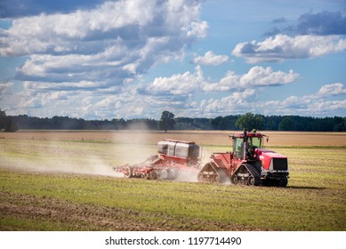 Agricultural Background With Red Tractor Pulling Plow, Throwing Dust In Air. Combine Harvester At Wheat Field. Heavy Machinery During Cultivation, Working On Fields. Dramatic Sky, Rain, Storm Clouds
