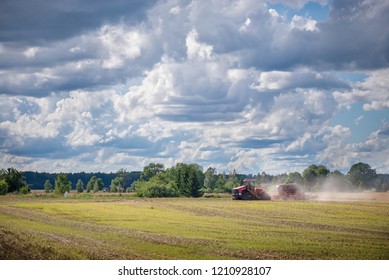 Agricultural Background With Red Tractor Pulling Plow, Throwing Dust In Air. Combine Harvester At Wheat Field. Heavy Machinery During Cultivation, Working On Fields. Dramatic Sky, Rain, Storm Clouds
