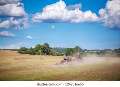 Agricultural Background With Red Tractor Pulling Plow, Throwing Dust In Air. Combine Harvester At Wheat Field. Heavy Machinery During Cultivation, Working On Fields. Dramatic Sky, Rain, Storm Clouds
