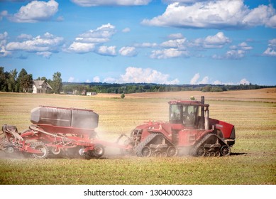 Agricultural Background With Red Tractor Pulling Plow, Throwing Dust In Air. Combine Harvester At Wheat Field. Heavy Machinery During Cultivation, Working On Fields. Dramatic Sky, Rain, Storm Clouds
