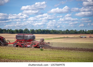 Agricultural Background With Red Tractor Pulling Plow, Throwing Dust In Air. Combine Harvester At Wheat Field. Heavy Machinery During Cultivation, Working On Fields. Dramatic Sky, Rain, Storm Clouds
