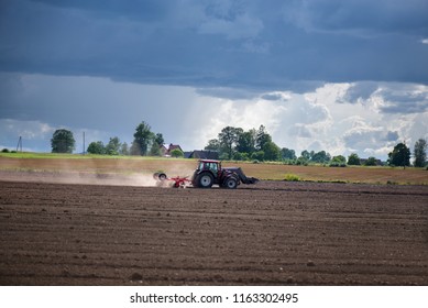 Agricultural Background. Tractor Pulling Plow, Throwing Dust In Air. Combine Harvester At Wheat Field. Heavy Machinery During Cultivation, Working On Fields. Dramatic Sky, Sun Rays, Rain, Storm Clouds