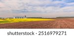 Agricultural fields and granaries on the horizon. Panoramic image of a field of plowed arable land and a field of yellow flowering rapeseed