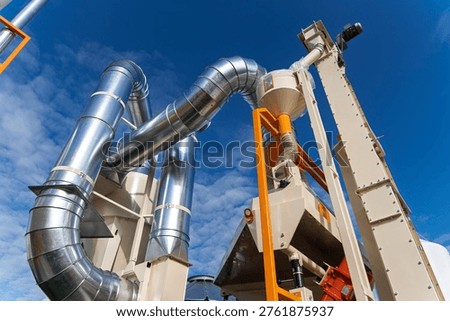 Agricultural grain processing facility with vertical bucket elevator and galvanized steel ventilation pipes against a blue sky, industrial crop handling system. High quality photo