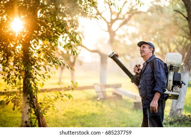 Agricultural industrial details with farmer using sprayer machine for pesticide control in fruit orchard during sunset time