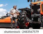 Agricultural machinery dealership. Man with digital tablet in hands looking at farm tractor.