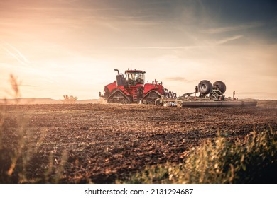 Agricultural modern red tractor with seeding into the soil after combine harvest using GPS for precision farming in the fields of Eastern Europe farm during colorful sunset.