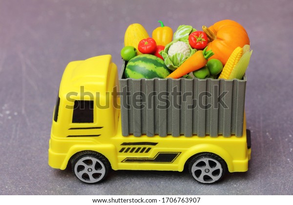 agricultural\
products transportation. A yellow toy truck delivering  fresh\
fruits and vegetables  in a\
container.