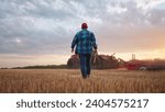 agriculture. farmer walk works in a field next to a tractor that plows the land. business agriculture concept. farmer with tablet works in field next to a tractor at farm sunset mowed wheat plows