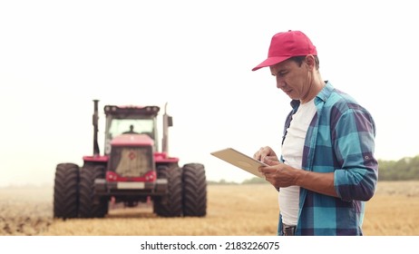 Agriculture. farmer working on a digital tablet in a field in the background tractor plows ground in a field of wheat. farming agriculture concept. business farmer in the field - Shutterstock ID 2183226075