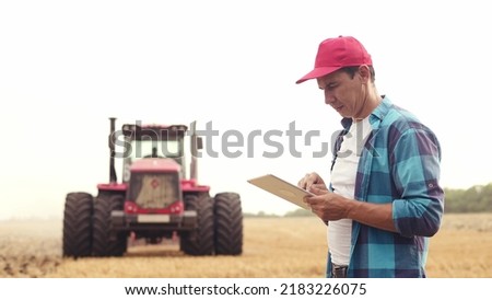 Agriculture. farmer working on a digital tablet in a field in the background tractor plows ground in a field of wheat. farming agriculture concept. business farmer in the field