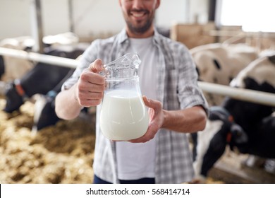 agriculture industry, farming, people and animal husbandry concept - happy smiling young man or farmer with cows milk in jug at cowshed on dairy farm - Shutterstock ID 568414714
