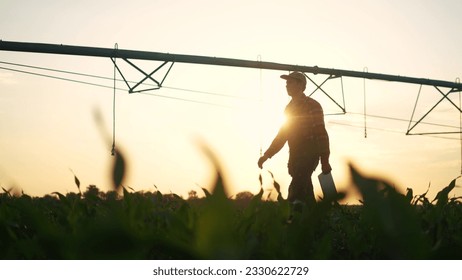 agriculture irrigation. silhouette farmer with a tablet walks through field with corn and a plant for irrigating the field with water. irrigation business agriculture concept. irrigation corn - Shutterstock ID 2330622729