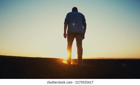 Agriculture. A Male Farmer In Rubber Boots Walks On A Plowed Agricultural Floor. Farm Worker Walking Home After Harvest At The End Of The Working Day Legs In Rubber Boots Agriculture Sun