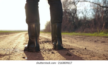 agriculture. man farmer in rubber a boots walk along road near a black field. man farmer worker walk home after harvesting end of sunset the working day feet in rubber boots agriculture