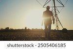 Agriculture. Silhouette of a farmer irrigating his corn. Agriculture field farm concept. Farmer goes to install irrigation. Silhouette of a farmer going for lifestyle irrigation with corn.